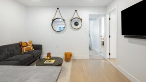 A modern living room with a gray sofa, a coffee table, and two wall-mounted mirrors. A flat-screen TV is mounted on the wall to the right.