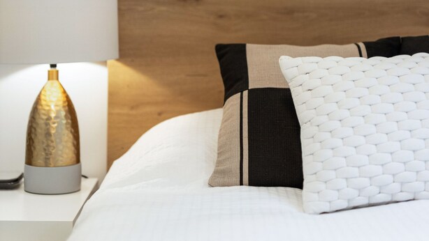 A neatly made bed with a wooden headboard, a lamp, and a textured wall hanging.