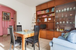 A dining area with a wooden table and chairs, a television, and a bookshelf with books and decorative items.