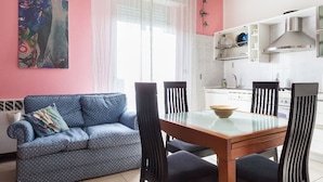 En stue med blå sofa, spisebord med stole, samt et køkken med hvide skabe og komfur.
