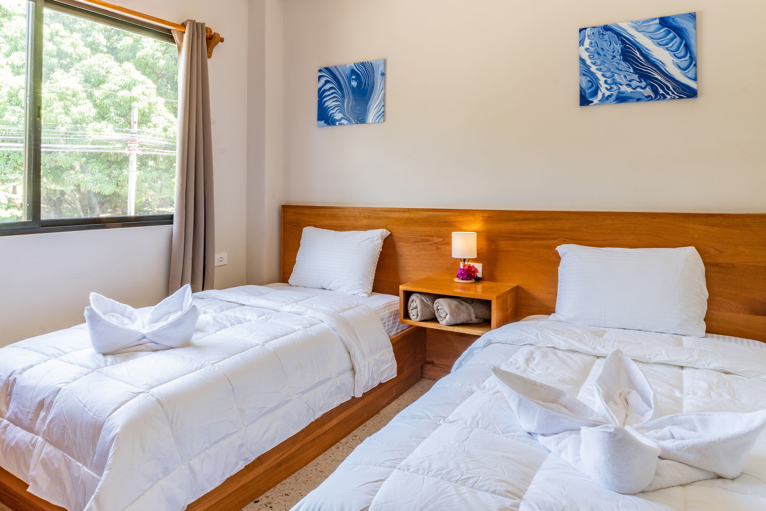 Een hotelkamer met twee bedden, een houten hoofdbord, een nachtkastje met een lamp en kunstwerken aan de wanden.