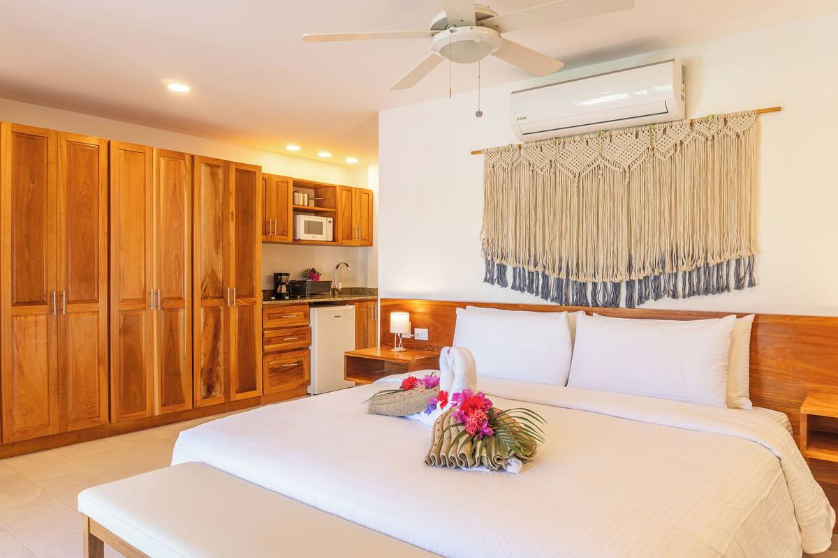A hotel room with a bed, wooden cabinets, a kitchenette, and a ceiling fan.