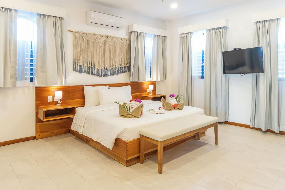 A hotel room with a wooden bed, a bench, a TV, and a wall-mounted air conditioner.