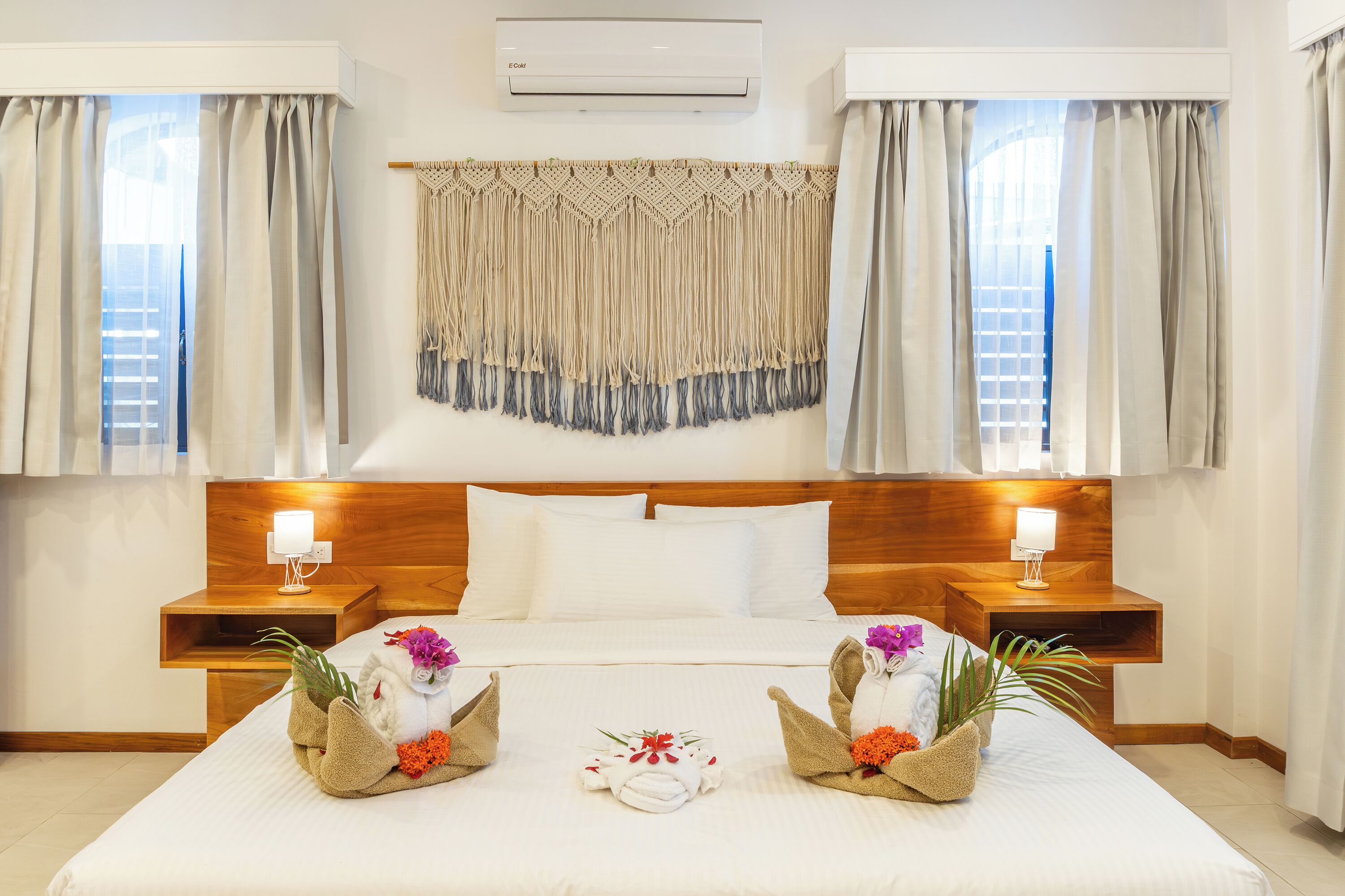 A hotel room with a large bed, wooden headboard, two bedside tables with lamps, and a wall-mounted air conditioner.
