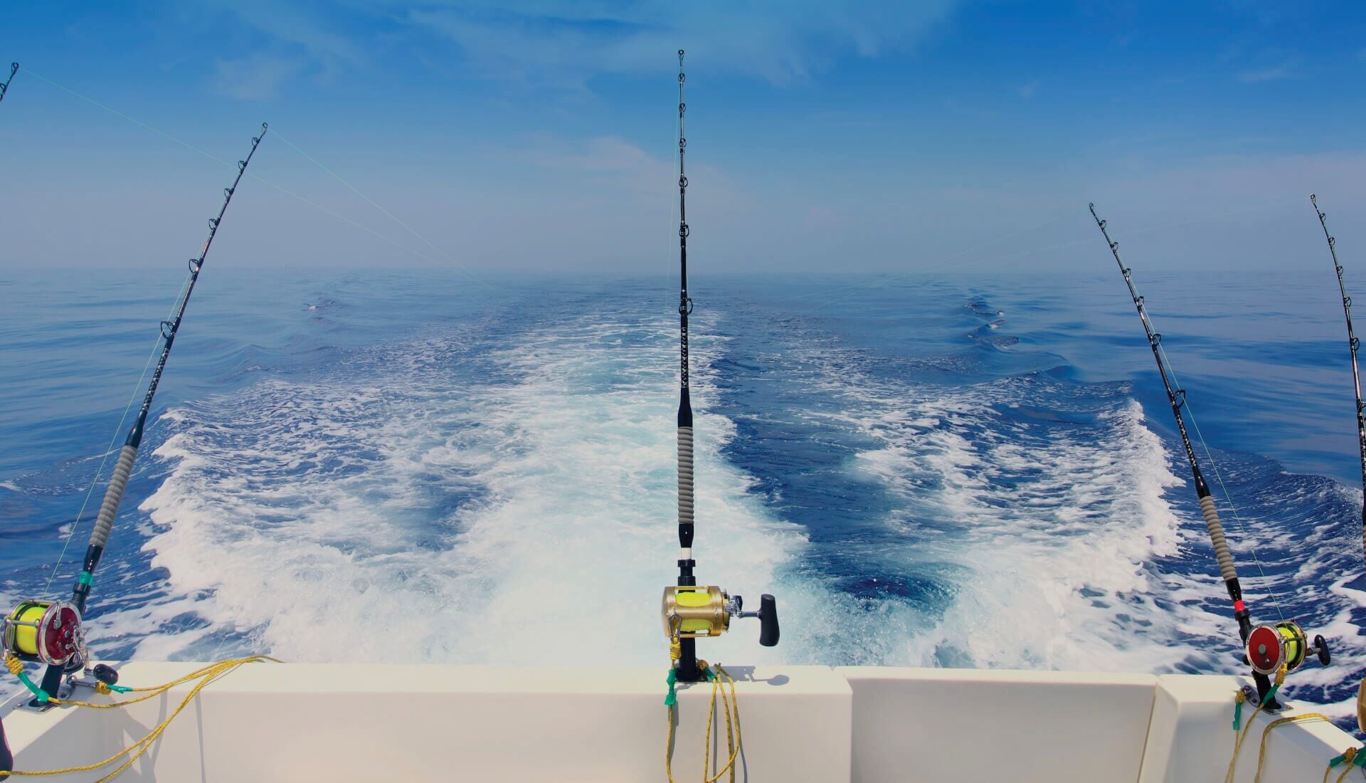 A boat with three fishing rods and a reel, set against a backdrop of open water and waves.