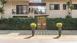 Un edificio moderno con un área de estar al aire libre cubierta, una entrada protegida por una reja y un camino de baldosas.