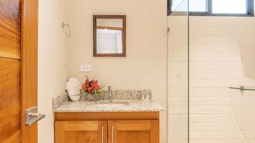 A bathroom with a wooden vanity, a glass shower enclosure, and a small window above the mirror.