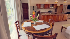 A dining area with a wooden table, white placemats, and chairs. A vase with flowers is on the table. - Residencias Samara (Sámara)