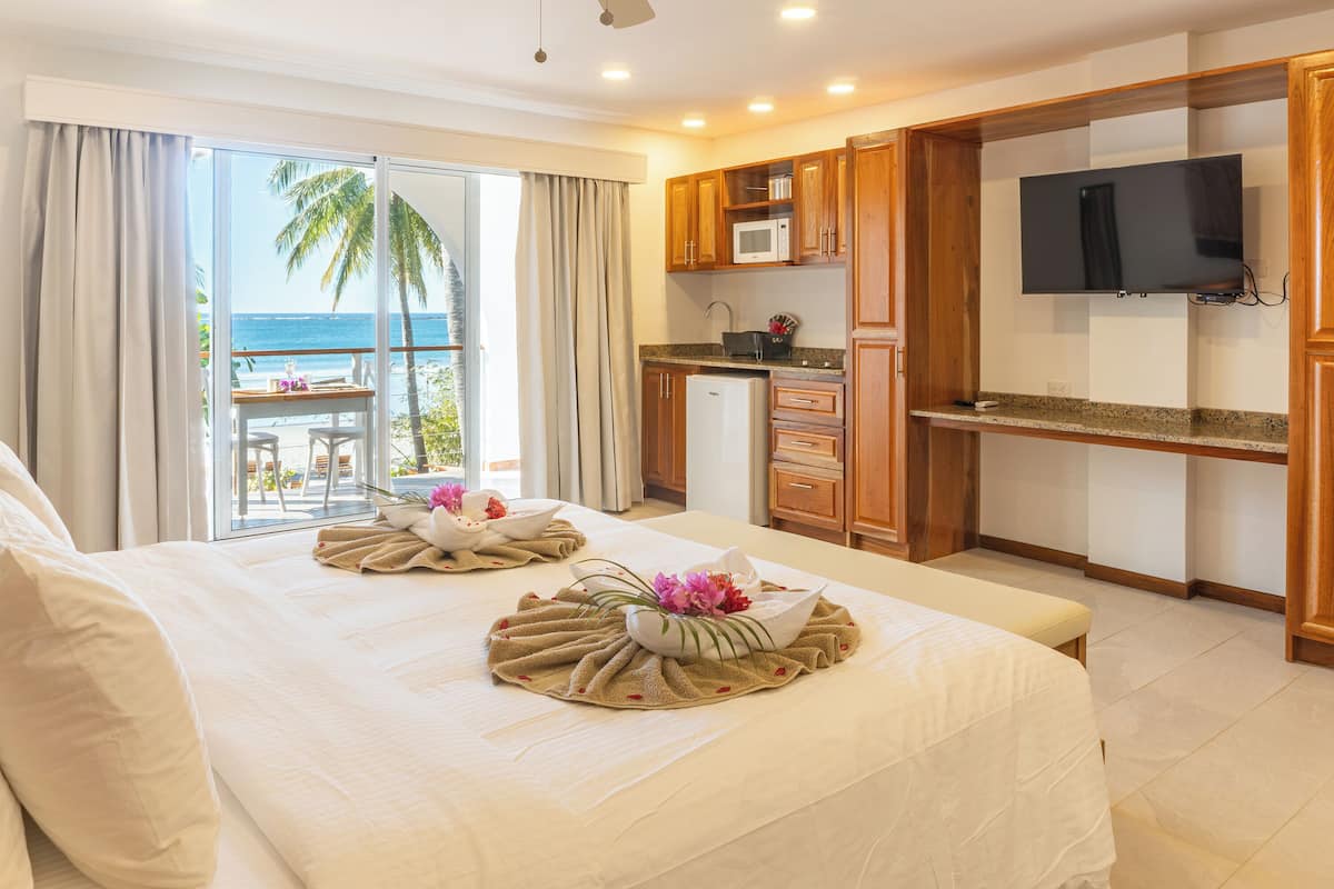 A hotel room with a balcony, a kitchen area, and a TV.