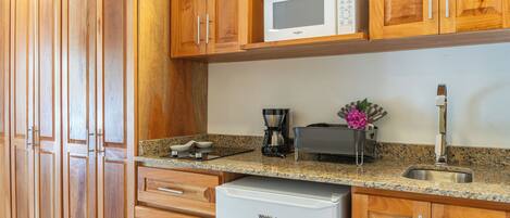 A kitchen with wooden cabinets, a microwave, a coffee maker, and a small refrigerator.