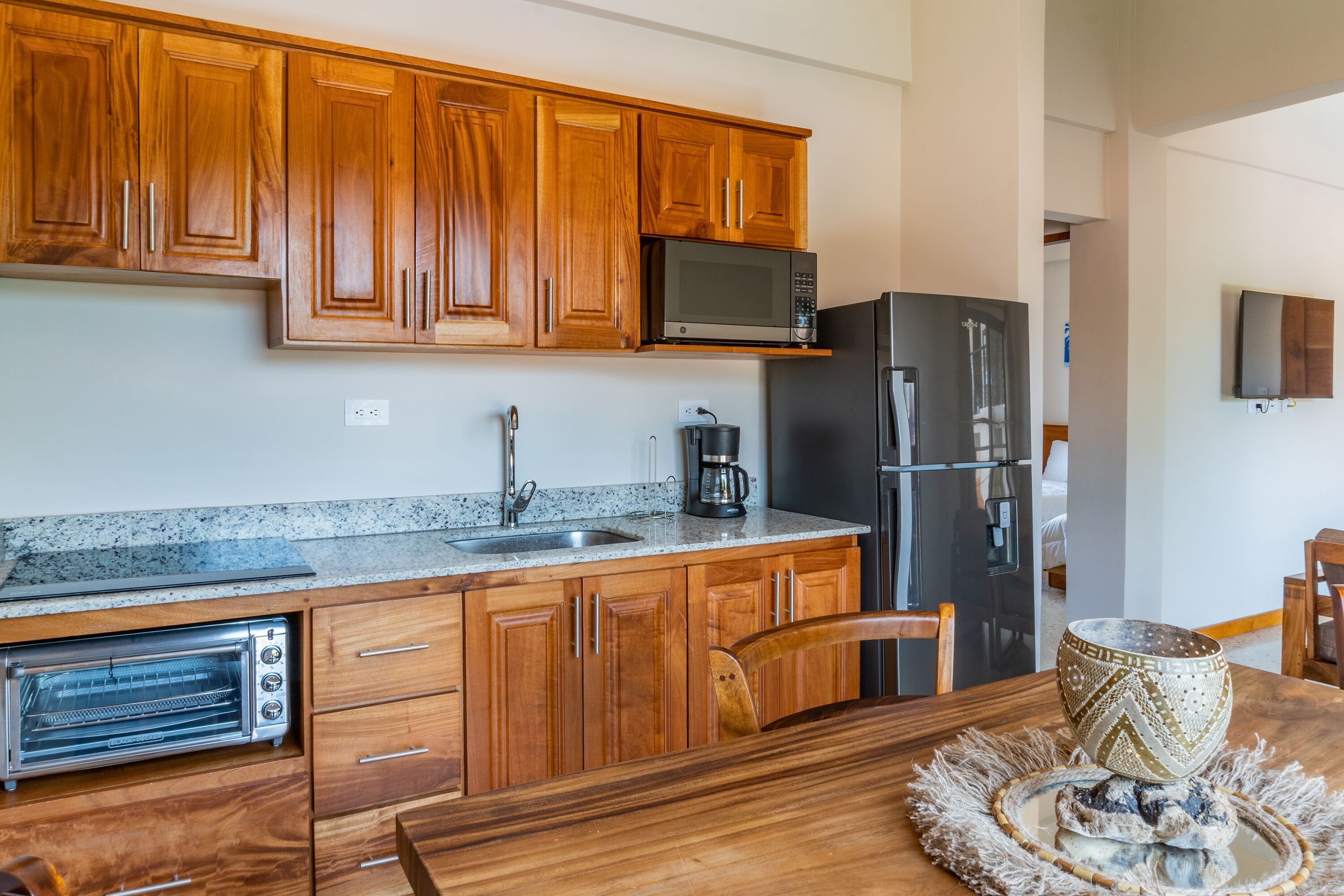 A kitchen with wooden cabinets, a microwave, a refrigerator, a toaster oven, and a coffee maker.
