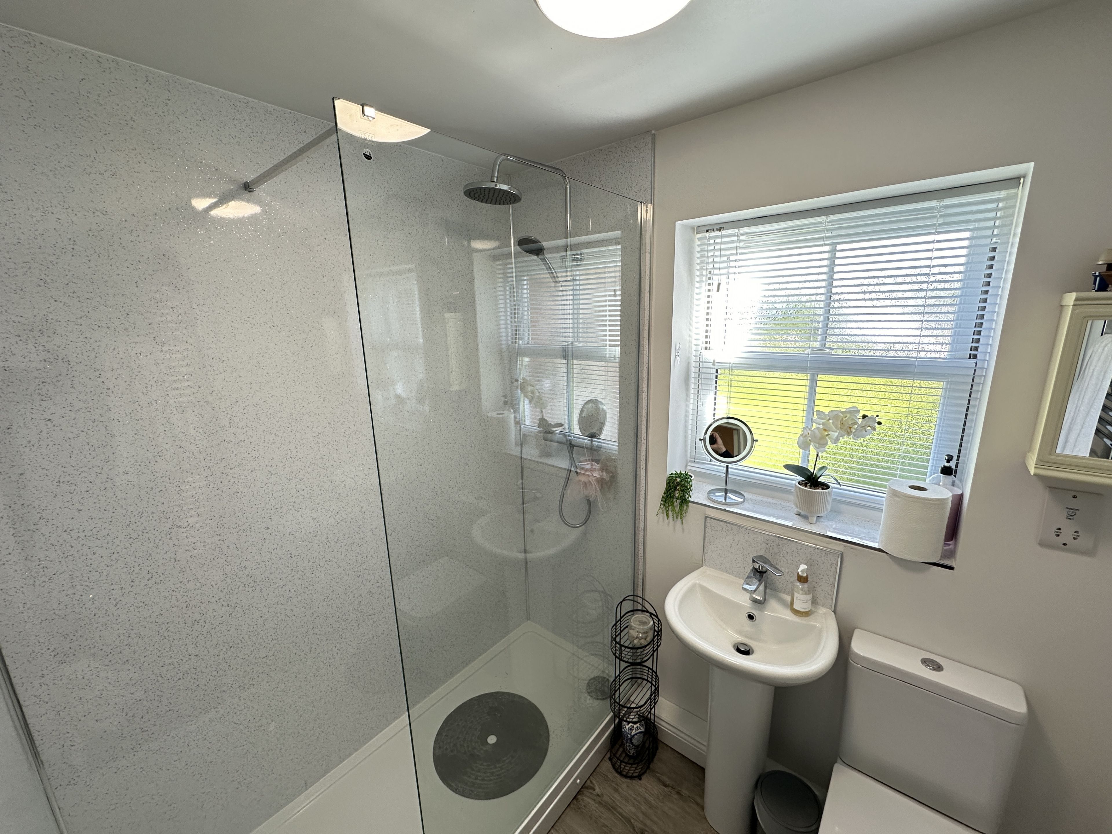 Een moderne badkamer met een douchecabine van glas, een wastafel met spiegel en een raam met zonwering.
