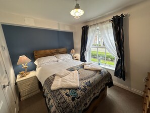 Un dormitorio con una cama grande, dos mesitas de noche, una lámpara y una ventana con cortinas.