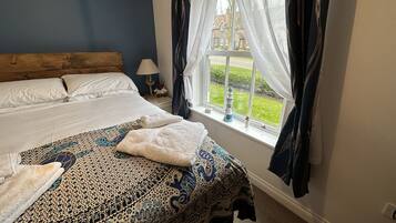 Un dormitorio con una cama grande, una mesita de noche con lámpara, una ventana con cortinas y vistas al exterior.