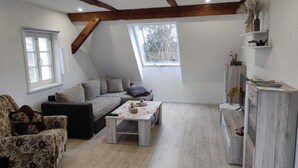 A cozy loft-style living space with a sloped ceiling, exposed wooden beams, a sofa, a coffee table, and a small desk area. - Vacation apartment in a renovated monument (max. 5 persons) (Bischofswerda)