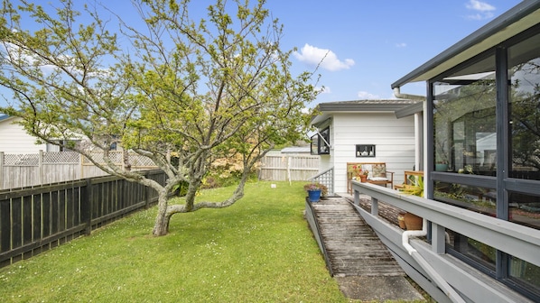 A modern house with a large glass window, a wooden deck, and a tree in the yard.