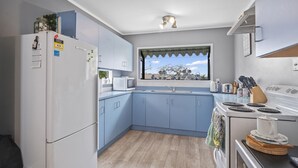 A compact kitchen with a refrigerator, microwave, sink, stove, and window with a view of trees. - Beachglen - Snells Beach Holiday Home (Snells Beach)