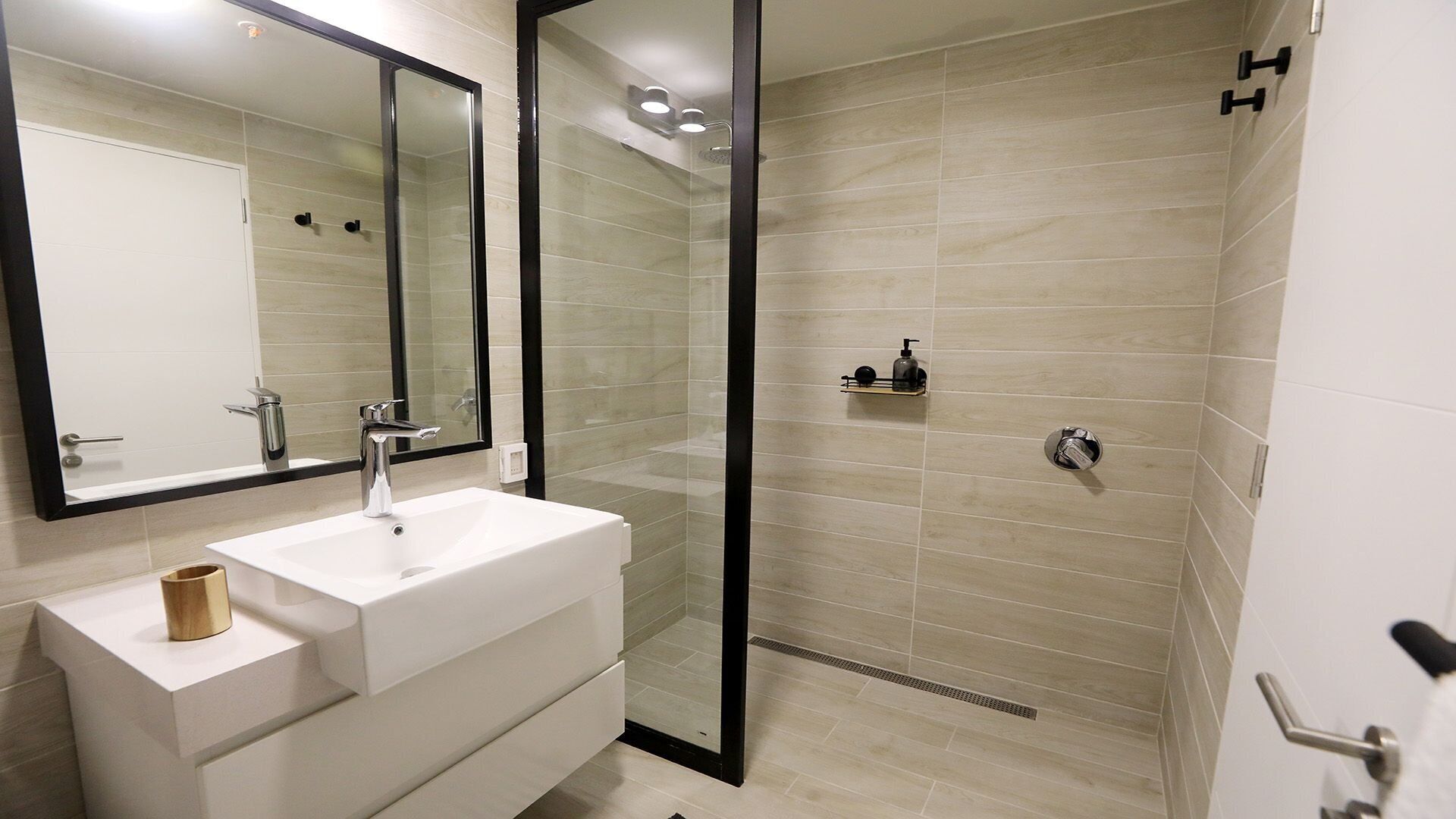 Un baño moderno con lavamanos blanco, un espejo grande y zona de ducha con mampara de vidrio.