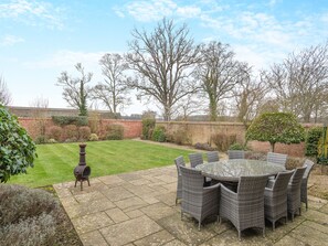 A patio with a round table and chairs, a barbecue grill, and a brick wall in the background.
