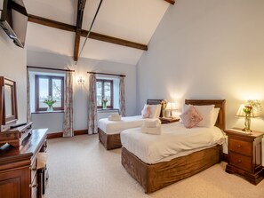 A bedroom with two beds, a wooden dresser, a desk, and a window with curtains.