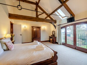 A bedroom with a large bed, wooden ceiling beams, a wardrobe, a vanity, and a balcony with a view.