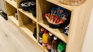 Un mueble de madera con un televisor, una cesta de frutas, paquetes de aperitivos y botellas de bebidas.