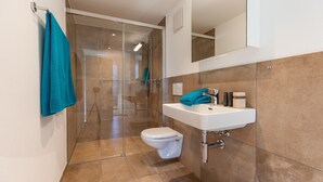 Un baño moderno con cabina de ducha de vidrio, un lavabo blanco y un inodoro.