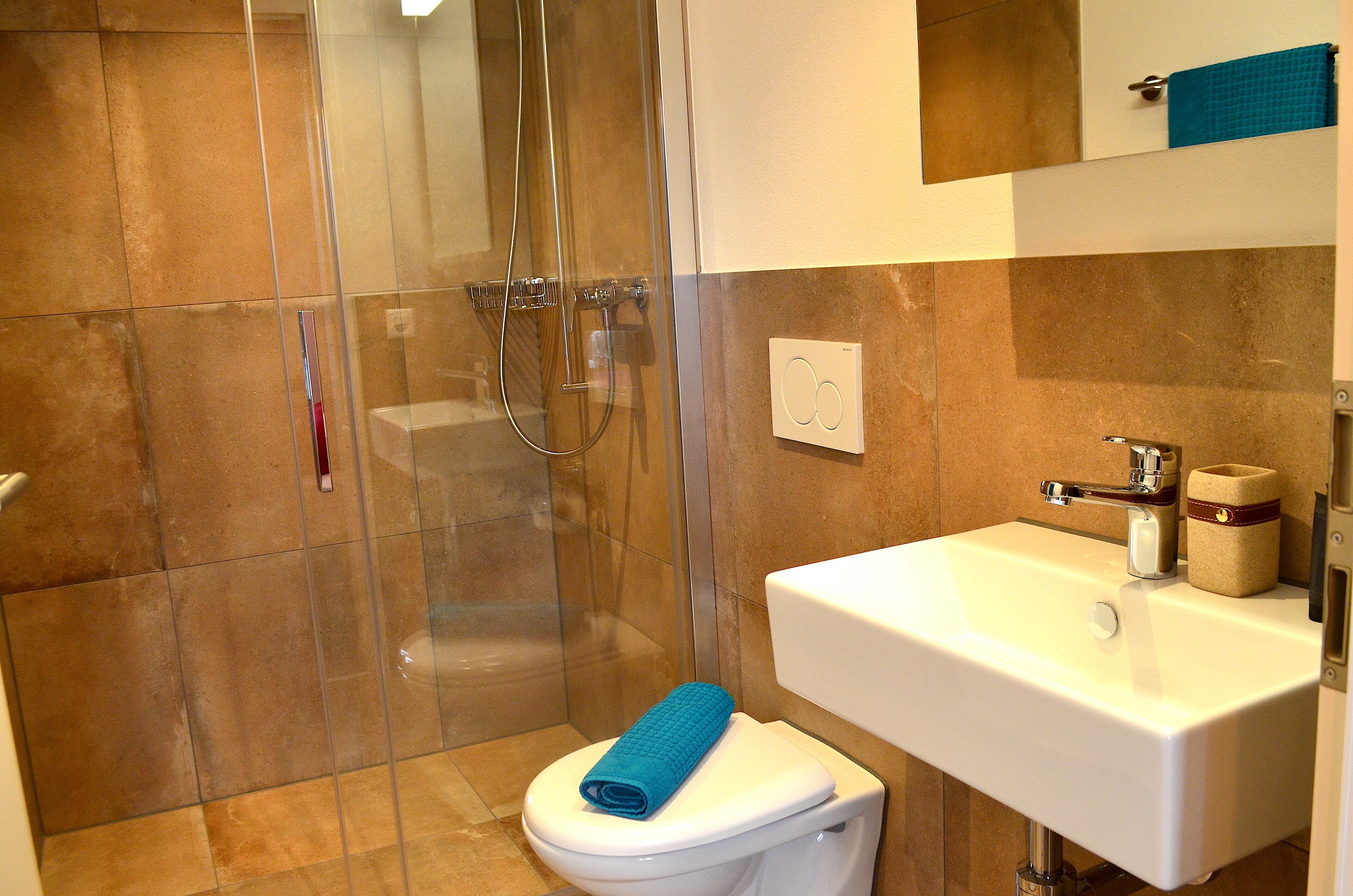 Une salle de bain avec une douche à parois de verre, un lavabo blanc et des toilettes avec une serviette bleue.