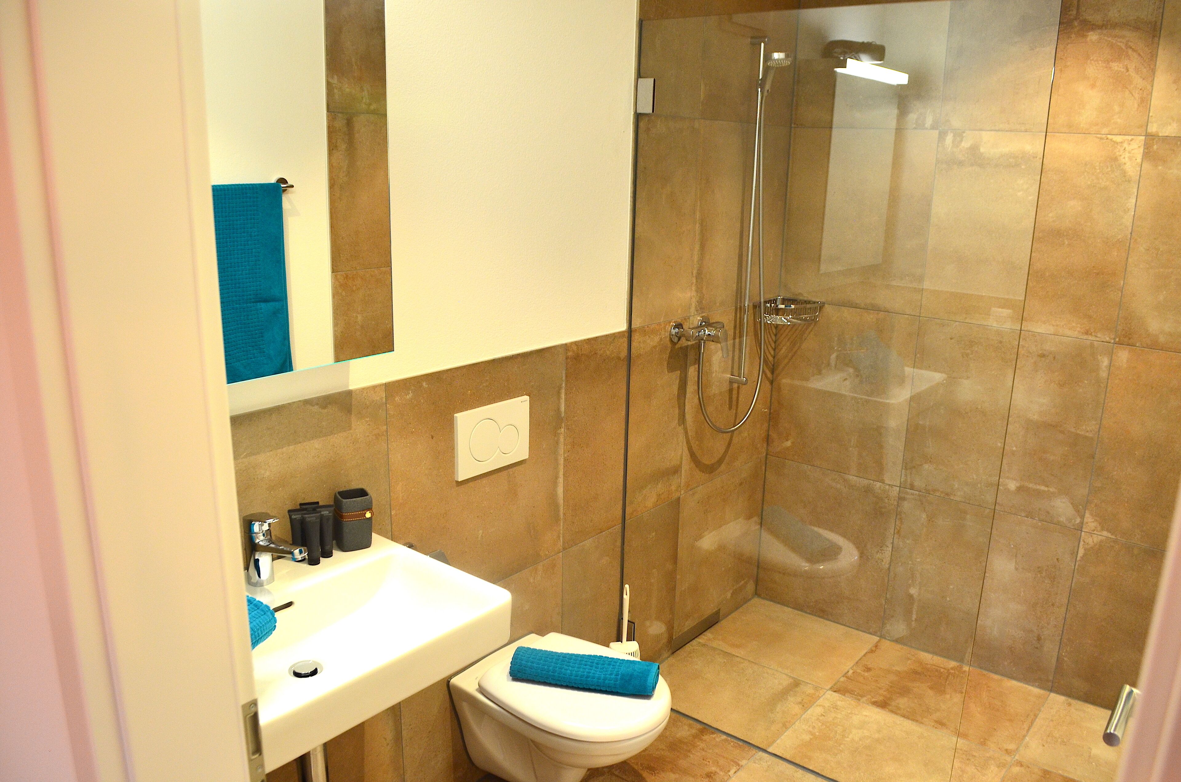 Un baño con un lavamanos blanco, un inodoro y una zona de ducha con mampara de vidrio.