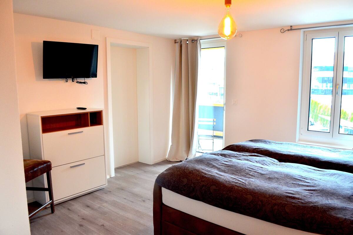 A bedroom with a bed, a TV, a desk, and a window.