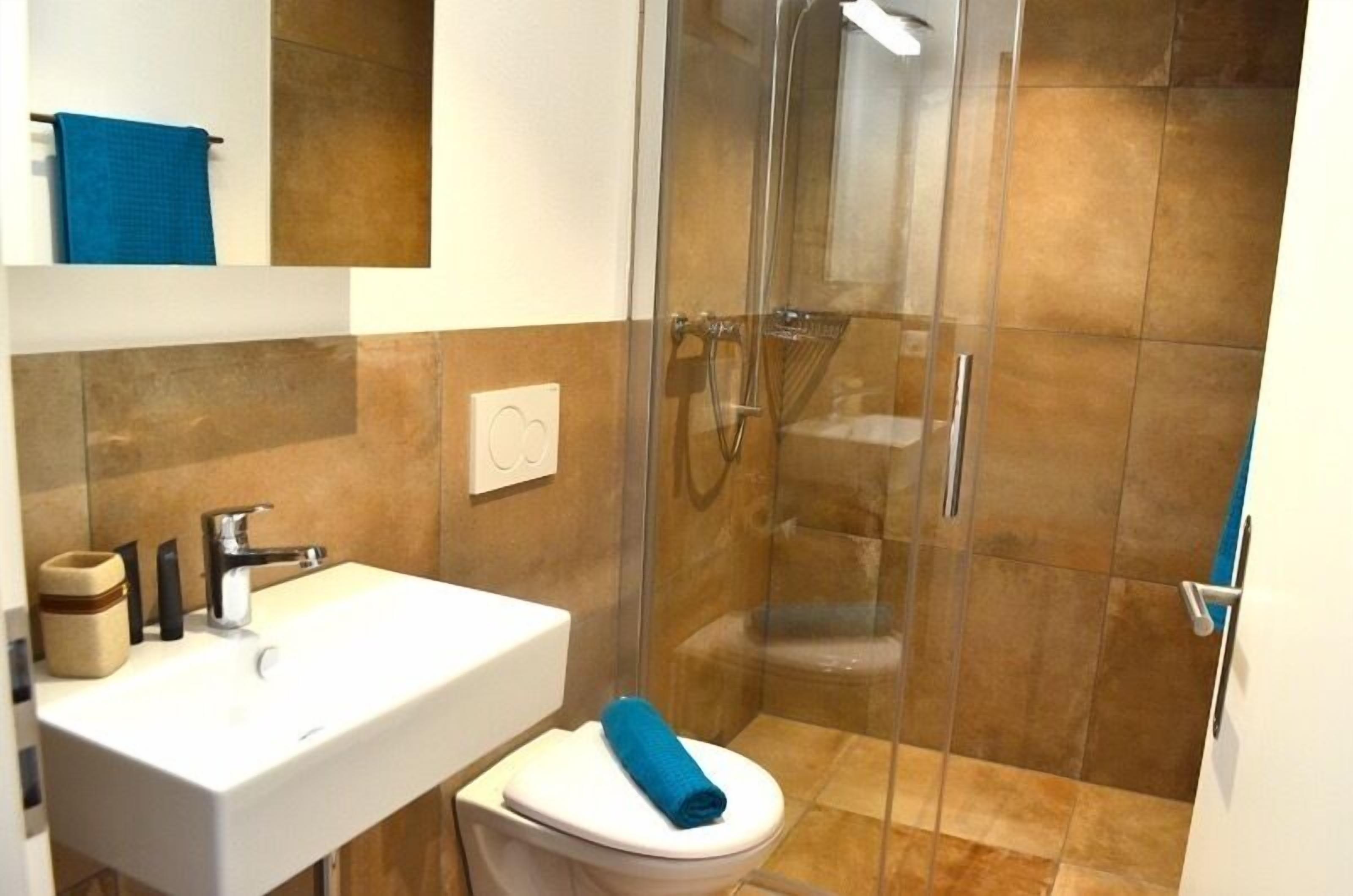 Un baño con ducha envuelta en vidrio, un lavamanos blanco y un inodoro con una toalla azul.