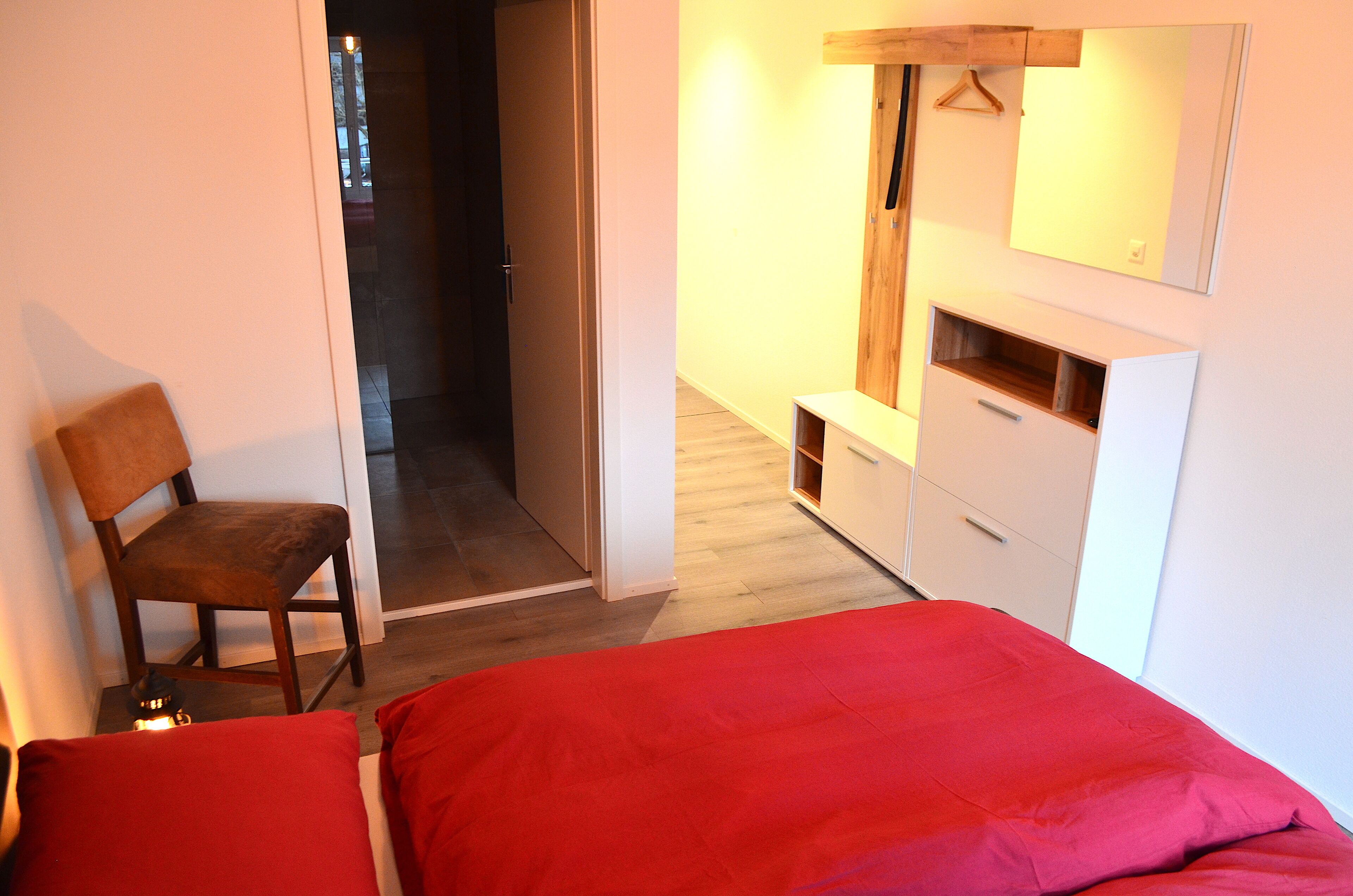 Un dormitorio con cama, una silla, armario y espejo.