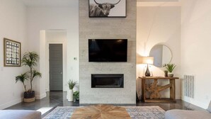 A modern living room with a fireplace, a mounted TV, and a round mirror. - Almanzo: Private Pool + Golf + Sand Dunes (Hurricane)