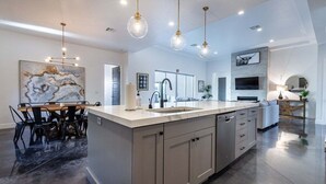 A modern kitchen with a large island, pendant lighting, and a dining area with a marble table. - Almanzo: Private Pool + Golf + Sand Dunes (Hurricane)