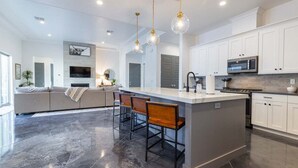 A modern kitchen with a central island, bar stools, and white cabinetry. - Almanzo: Private Pool + Golf + Sand Dunes (Hurricane)