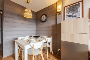 Een eetgedeelte met een houten tafel, witte stoelen, een zwarte kom en een wandklok.