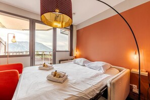 Een hotelkamer met een bed, een rode stoel, een groot raam en uitzicht op bergen.