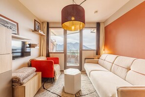 Een moderne woonkamer met een bank, fauteuils, een televisie en een groot raam met uitzicht op de bergen.