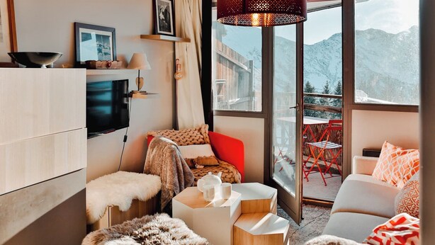 Un salon moderne doté d’un téléviseur, de sièges confortables, d’une cheminée et d’une grande fenêtre offrant une vue sur les montagnes.