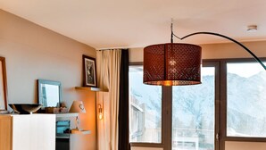 Un salon moderne avec un canapé, un pouf et un téléviseur. Une grande fenêtre offre une vue sur les montagnes.