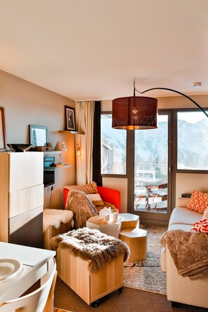 Un salon moderne avec une grande fenêtre, un canapé rouge, un fauteuil blanc et un meuble en bois.