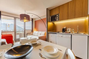 Een moderne keuken met een magnetron, koffieapparaat en een spoelbak. Er is een eethoek met een tafel gedekt voor twee personen, en een bank op de achtergrond.