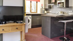 Uma cozinha compacta com máquina de lavar, micro-ondas e um espaço bar com banquetas.