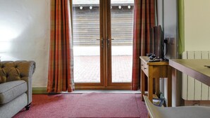 Quarto com porta de vidro deslizante, um sofá, uma mesa de madeira com televisão e um relógio na parede.