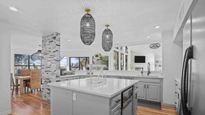 Una cocina moderna con una isla grande, electrodomésticos de acero inoxidable y un comedor con sillas de mimbre.