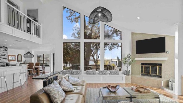 Un salón amplio con un ventanal grande, una chimenea y una cocina visible al fondo.