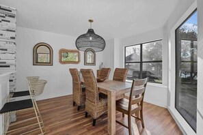 A dining area with a wooden table and wicker chairs, a black pendant light, and a large window with a view of the outside. - Huge Lakefront Getaway Hot Tub, Deck, Sleeps 16 (Little Elm)