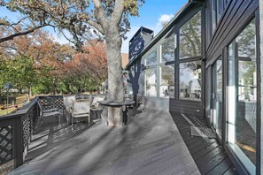 A wooden deck with outdoor furniture, a tree, and a building with large windows. - Huge Lakefront Getaway Hot Tub, Deck, Sleeps 16 (Little Elm)