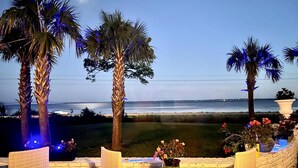 A patio with wicker chairs and a table, overlooking a beach with palm trees and a view of the ocean. - Eden Guest House on Bayfront Mansion Estate. A 3/3! 20 scenic minutes to Destin (Freeport)