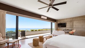 Une chambre d’hôtel moderne dotée d’un grand lit, d’un ventilateur de plafond, d’une télévision et d’un balcon offrant une vue sur l’océan.